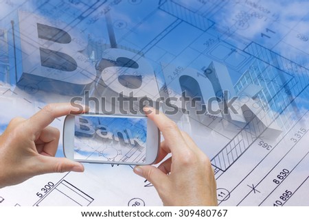In the bottom left of the photo are hands holding smart phone, whose screen contains photo of the bank inscription. Background of the photo contains abstract of the blueprint and bank inscription.