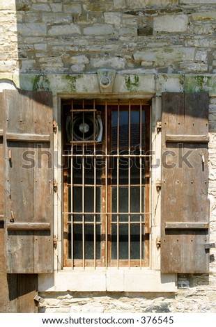 brown shutters open on an old barred window in a mediterranean village