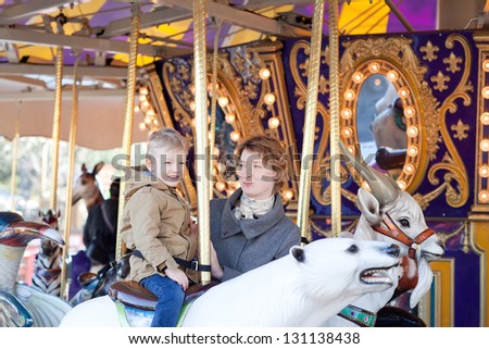adorable little boy riding the merry-go-round with his mother