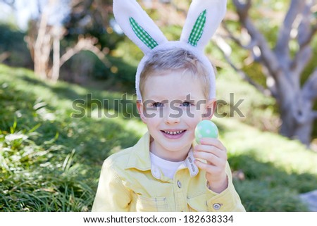 happy smiling boy with bunny ears holding easter egg at spring time
