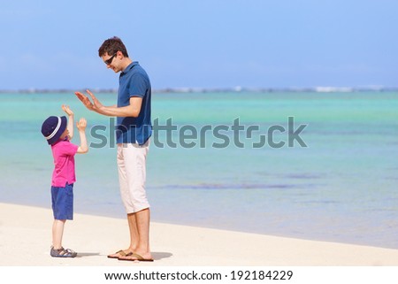 little boy giving his father high five at the beach, spending fun day together during summer vacation