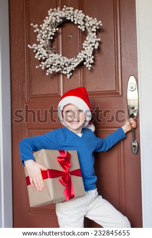 smiling cheerful boy with christmas present by the decorated house