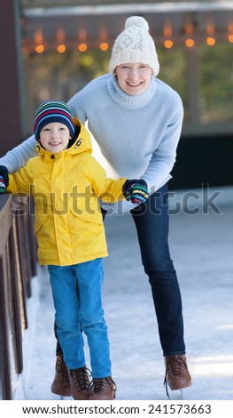 young mother and her son ice skating together at outdoor skating rink at winter