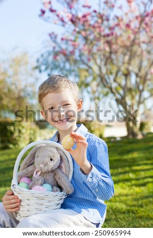 cute little boy with basket full of eggs and plush bunny toy at easter and spring time with blooming magnolia in the background