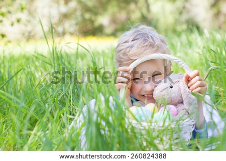 little smiling boy holding basket with easter eggs and bunny after egg hunt in the park lying in the grass