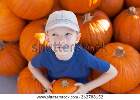 little excited kid looking up enjoying time at pumpkin patch sitting in the huge pile of pumpkins