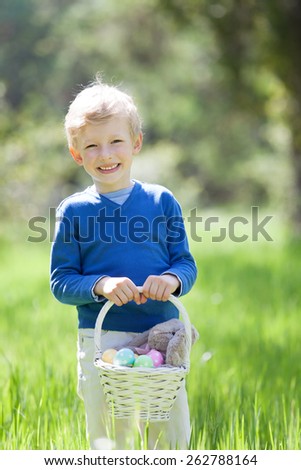 smiling little boy holding basket with easter eggs and bunny after egg hunt at spring time