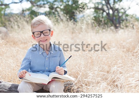 smart excited little boy in glasses studying with book and pencil ready for school, back to school concept