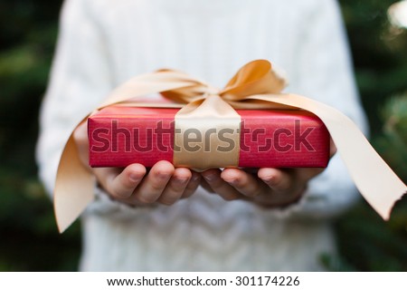 close-up of nicely wrapped christmas gift being held by a child with no face visible, christmas tree in the background, christmas time concept