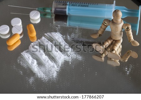Syringe, pills, blade and depiction of cocaine on mirror with wooden human figure