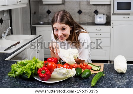 Woman making food in kitchen preparing salad holding lettuce head while smiling happy.
