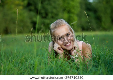 A happy laughing young woman laying on the grass and looking into the camera.