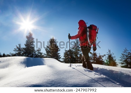 Winter hiking. A trekker, walking in the snow, takes a rest for admire the panorama. Sunny and frosty winter day. Italian Alps, Europe.