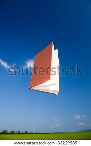 Flying book over a clear blue sky, vertical orientation. The text of the book is been blurred to avoid copyright issues.