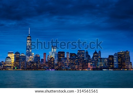 New York City Manhattan downtown skyline at night with illuminated skyscrapers and cloudy sky.
