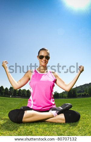 Young woman on the freshly cut grass stretching after exercise