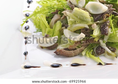 Salad from slices of the fried beef, quail eggs, sauce from olive oil of balsam vinegar on a light plate. A shot horizontal, focus in the center a shot
