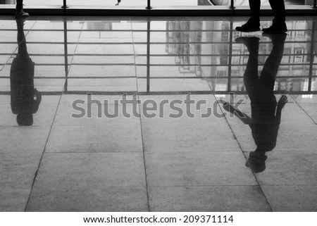 a woman stand along and a man walking on marble flooring with shadow reflection