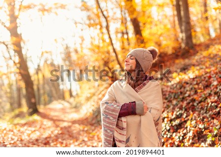 Beautiful young woman enjoying sunny autumn day in nature, walking down the forest path covered with colorful fallen leaves and relaxing, taking a breath of fresh air