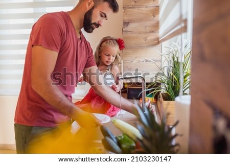 Beautiful little girl sitting at kitchen counter, having fun doing the washing up with her father in the kitchen after lunch Stock foto © 