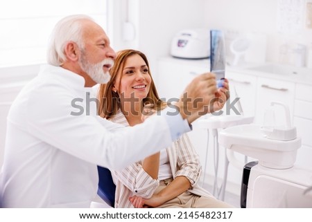 Dentist explaining necessary procedures to patient sitting in dental chair while looking at jaw x-ray at stomatology clinic ストックフォト © 