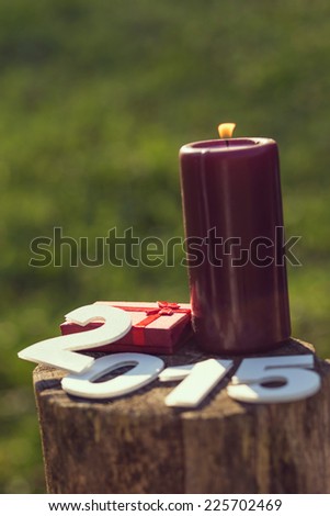 Lit Christmas candle with cardboard numbers 2015 and a present, outdoor
