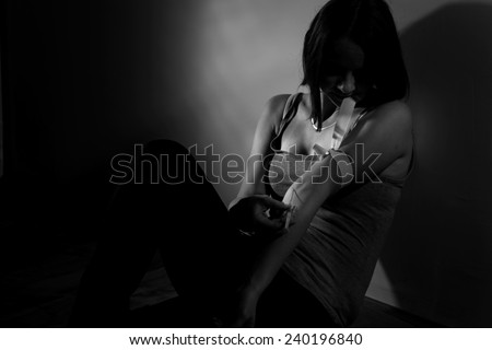 Young drug addict sitting on the floor, taking intravenous dose of heroin