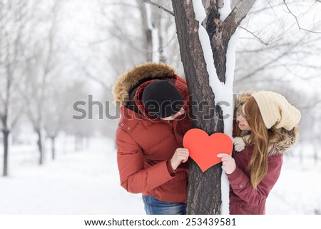 Couple in love looking at each other, holding red heart, standing next to a three