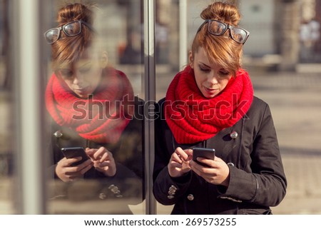 Beautiful young girl standing next to a shop window and typing a text message on her smart phone