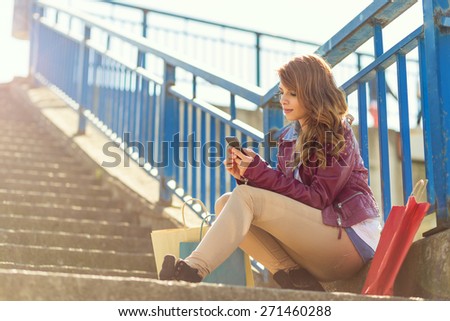 Young girl sitting on the stairs on a  beautiful sunny day, surfing the internet on her smart phone