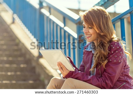 Young girl sitting on the stairs on a  beautiful sunny day, surfing the internet on her smart phone