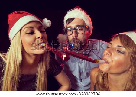 Three young friends having fun and blowing party whistles at New Year\'s Eve Celebration