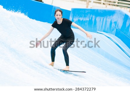 asia girl is playing surf borad with artificial waves house, action