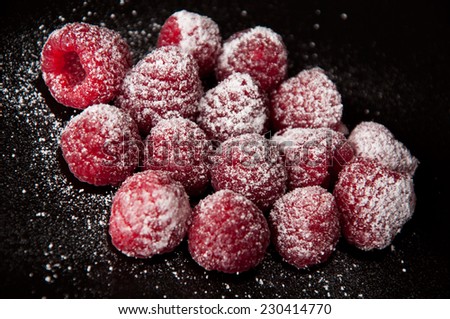 A group of beautiful red raspberries with a sugar powder on a black background