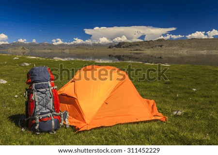 Tent camp and backpack on the side of the stream in the background of a mountain landscape.