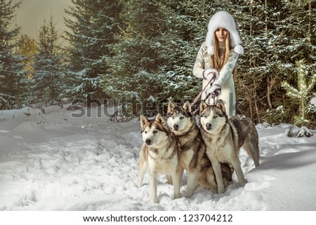 A portrait of beautiful woman with three dogs in winter forest