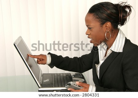 Smart african american woman points at computer screen, holding phone in hand