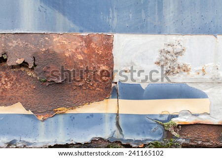 Beige Color strip on blue steel metal with water erosion drip, large yellow brown rust, color fade, crack, tears, green growth, and white aluminum section
