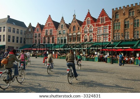 Row of vivid color houses at the paved square of the oldest town in europe brugge and cyclists drivindg on the square