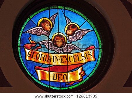 Round stained glass window of angel faces with Christmas message in Latin of Gloria in Excelsis Deo