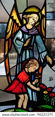 Stained glass window of guardian angel with little girl in red dress picking flowers