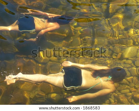 Two girls swimming underwater in a mountain pool.