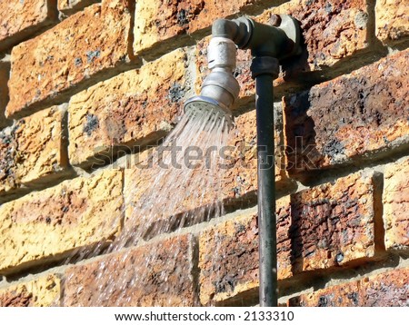 Outside shower with water spray mounted on a face brick wall.