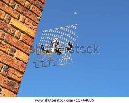 Television antenna mounted on a face brick wall juxtaposed against a blue sky and the moon.