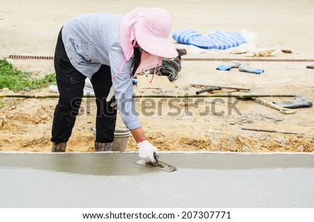 Women worker using trowel with wet concrete, Construction road with cement. Selective focus.