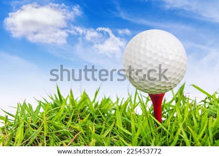 Golf ball on a tee against a blue sky and white clouds.
