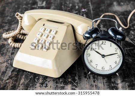 Retro clock and old telephone on wooden table.