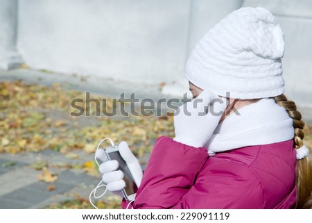 Girl child adjusts earphones talk on a cell autumn outdoors