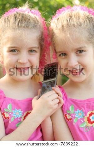 twin girls sharing a cell phone call vertical