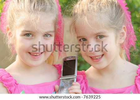 twin girls sharing a cell phone call